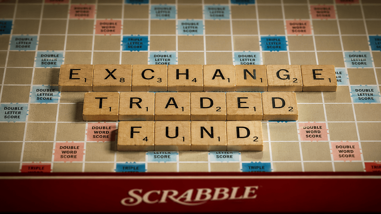 A close-up photo of a Scrabble board with wooden letter tiles spelling "EXCHANGE TRADED FUND" across three rows on the grid.