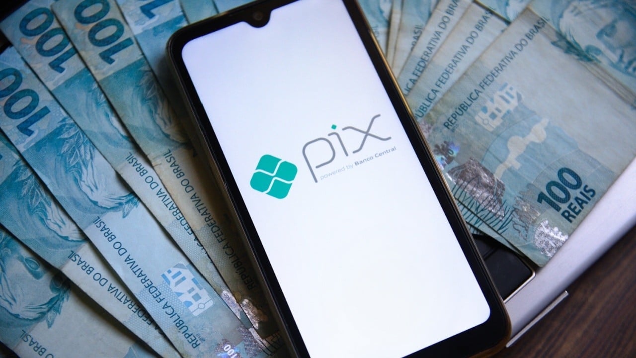 Pix logo in phone over Brazilian reais banknotes