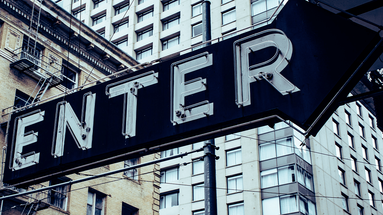 Vintage 'Enter' sign against a backdrop of urban high-rise buildings. - Photo credit Brett Sayles