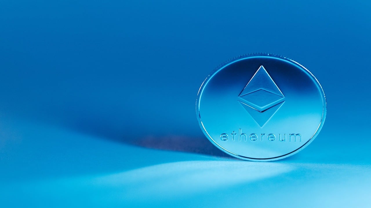 Ethereum logo on a coin placed against a bluish backdrop.