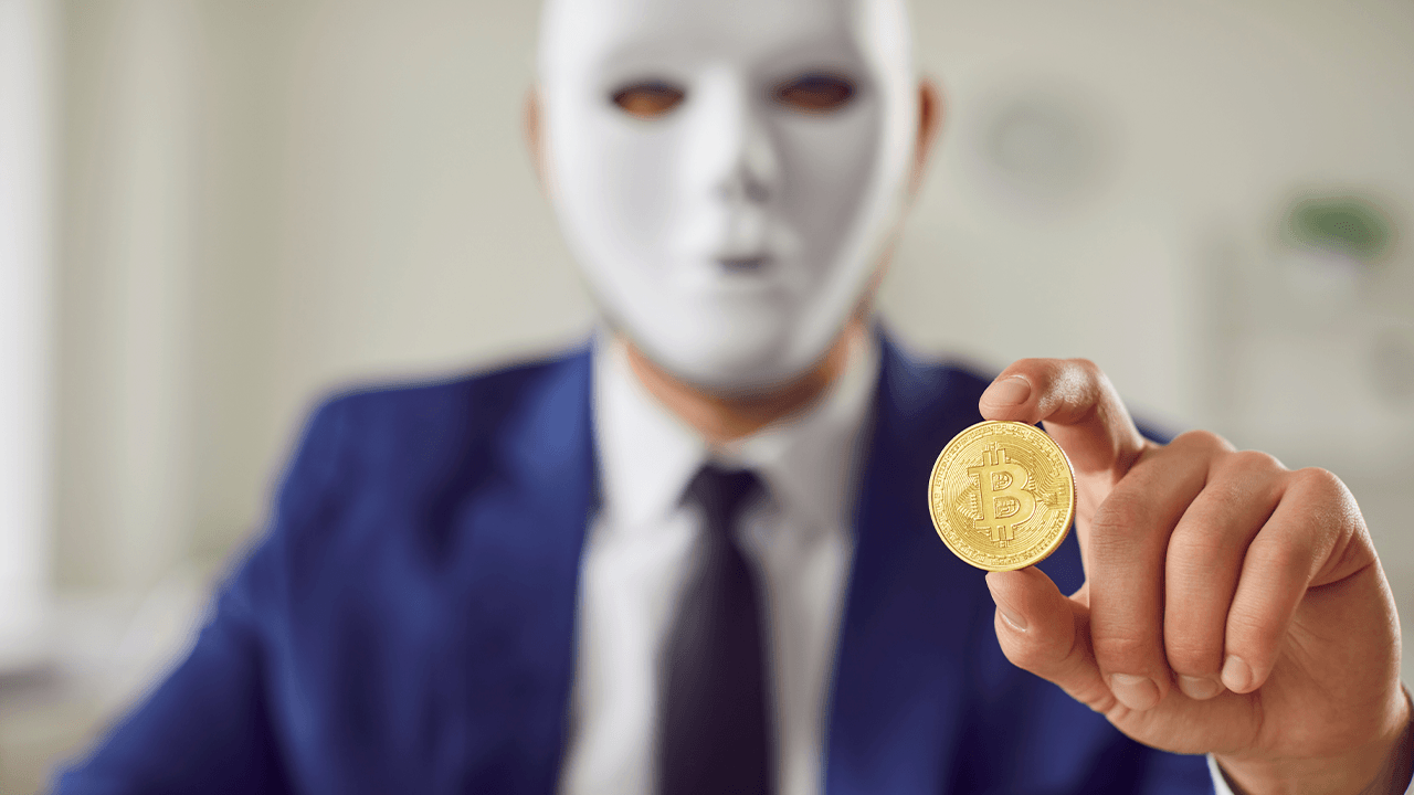 Man with a mask holding a physical bitcoin
